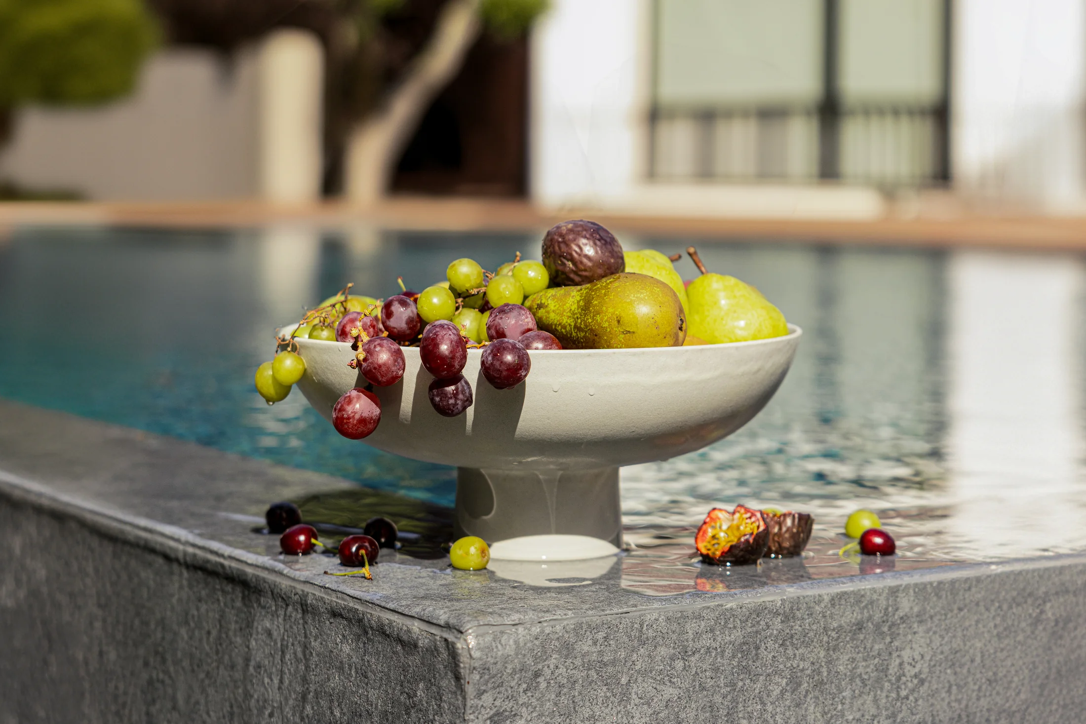 A ceramic pedestal bowl of fresh fruit at the water's edge